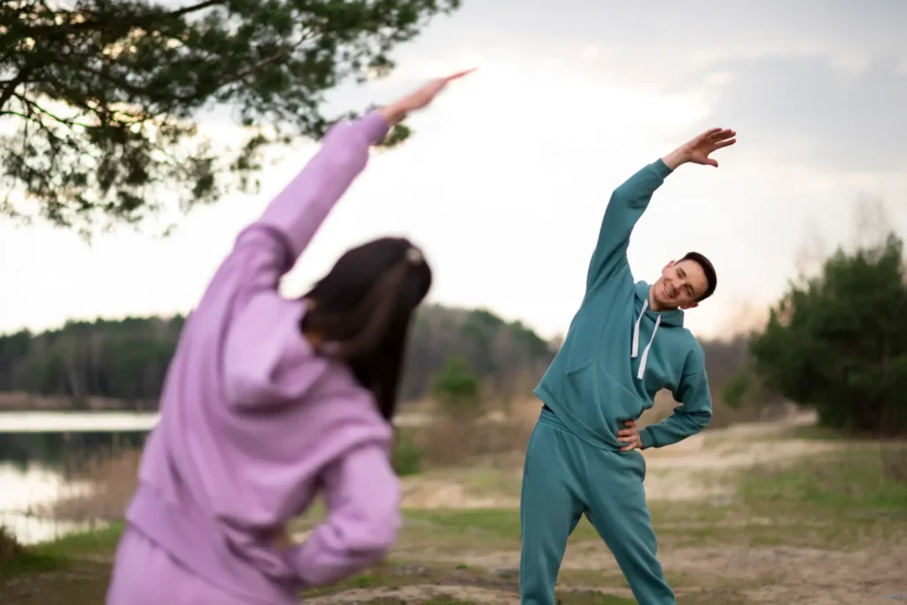 Two people practicing mindful movement stretches outdoors in nature to reduce stress and improve mental clarity.