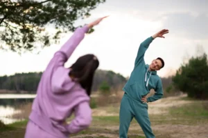 Two people practicing mindful movement stretches outdoors in nature to reduce stress and improve mental clarity.